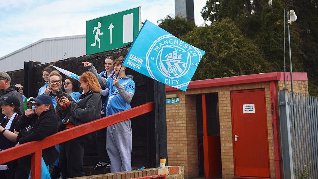 Man City fans stand in the away section at Chigwell Construction Stadium