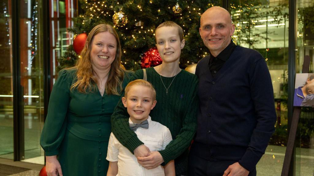 Liz Hatton, centre, stands with her mother (left), father (right) and little brother (front), in front of a Christmas tree decorated with lights and baubles.