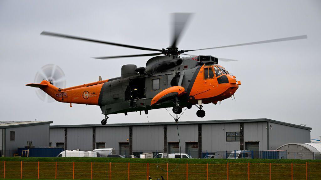 A yellow and black Sea King helicopter used for training by HeliOperations in flight.