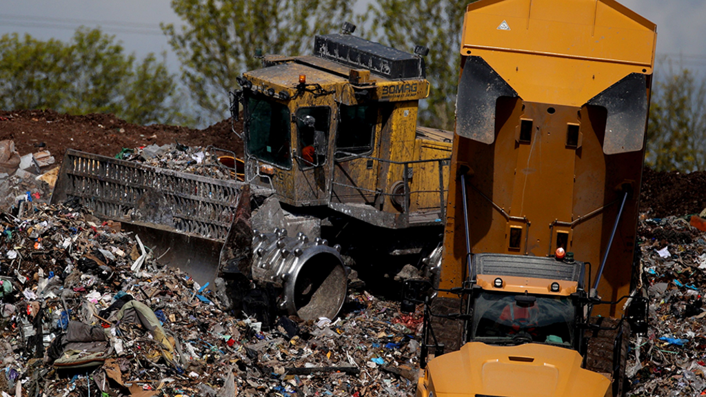 A bulldozer and tipper truck operating at a landfill site, moving rubbish