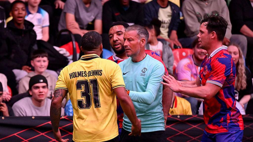 Troy Deeney stands behind referee Mark Clattenburg