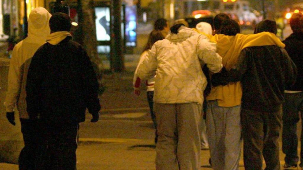 A group of young people wearing hoodies and sweatpants from the back. They're out on a Bristol street at night. The photo has a yellow tinge. 