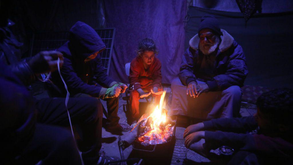 Displaced Palestinians warm themselves around a fire inside a makeshift shelter during cold weather in Deir al-Balah, central Gaza (25 February 2025)