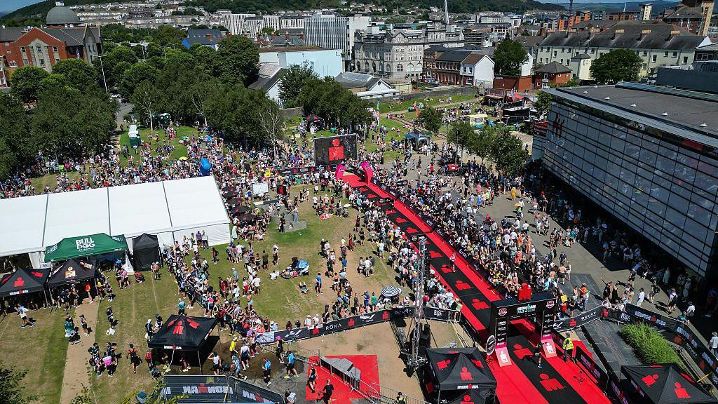 An aerial view of the finish line of Ironman 70.3 Swansea which is the first Pro Series race to be held in the UK. There are swarms of competitors and people watching on the with city skyline in the background