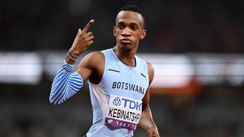 Collen Kebinatshipi shown from waist up wearing a Botswana sky blue sleeveless running jersey with his name written on a bib on the stomach, looks to his right while pointing his right index finger skywards as he prepares to compete in the men's 400m at the World Athletics Championships in Tokyo 