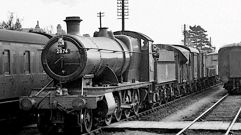 An old black and white image of the 2874 locomotive at work, with freight attached to the back