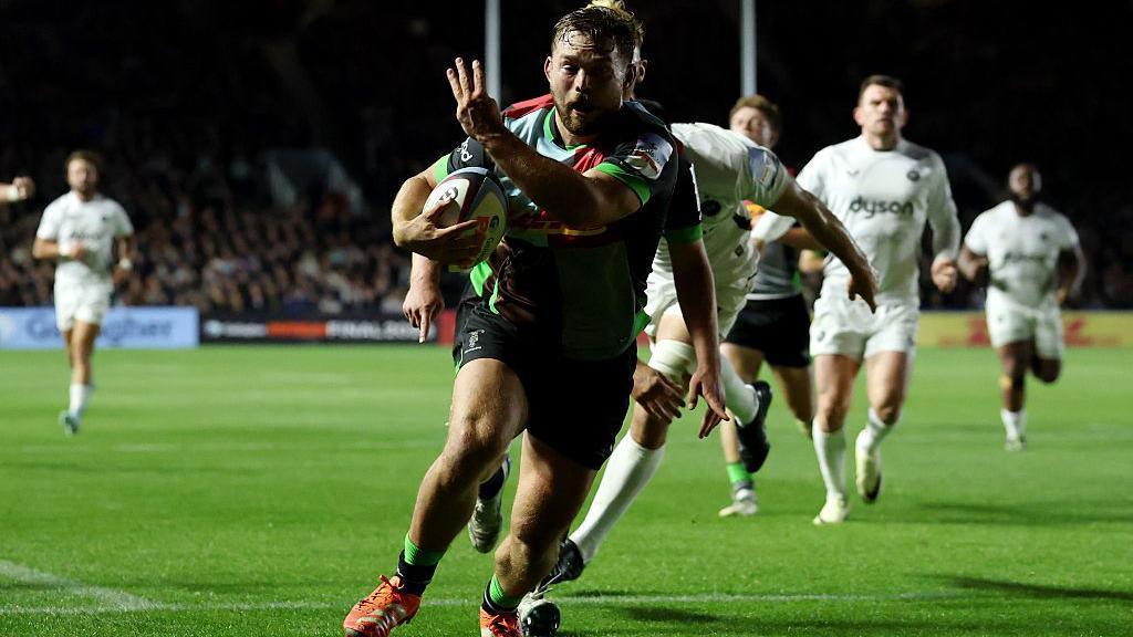 Will Evans runs over the line holding three fingers in the air to signify his three tries for Harelquins against Bath