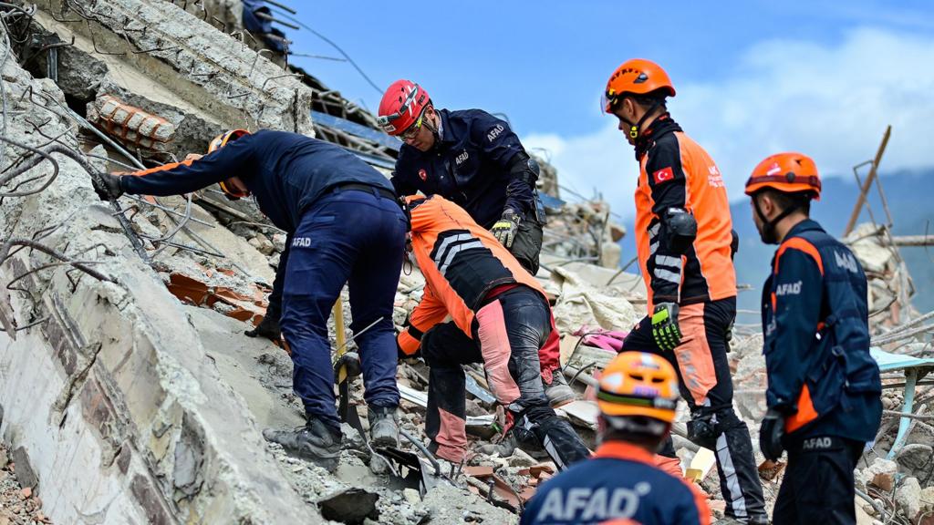 Turkish rescue teams in blue and orange work wear climb on top of building debris looking for survivors in La Guaira