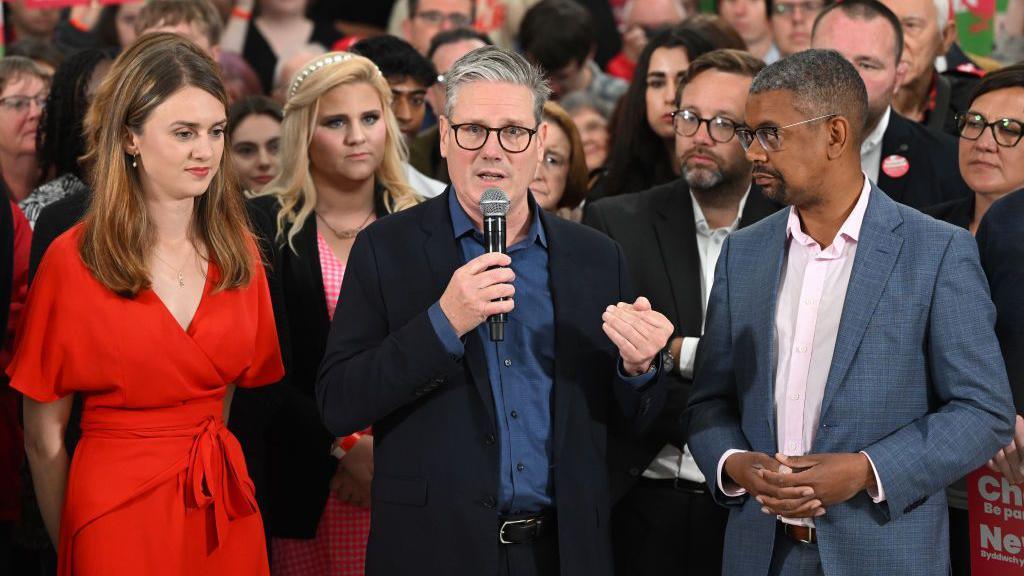 Labour Leader Sir Keir Starmer (C) stands next to parliamentary candidate for Carmarthenshire, Martha O'Neil (L), and First Minister of Wales, Vaughan Gething (R), as he speaks to supporters on the final day of campaigning at the West Regwm Farm on 3 July 2024 in Whitland