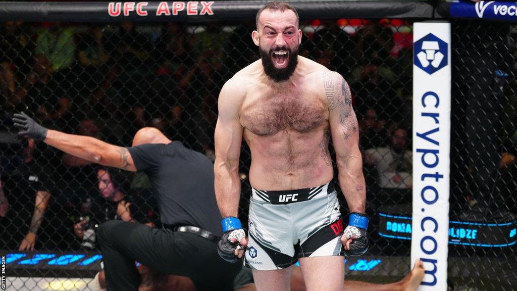 Roman Dolidze celebrates with the referee stopping a fight behind him