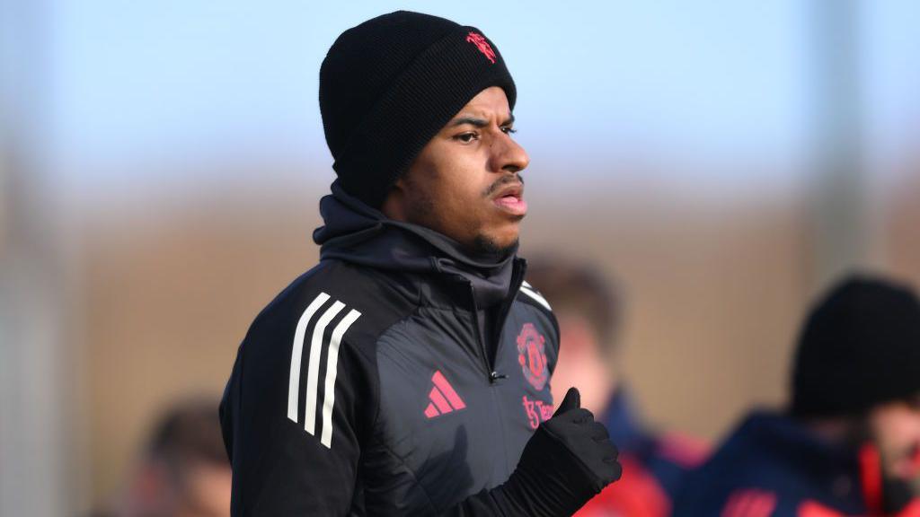 Marcus Rashford wearing a black hat, black gloves and black Manchester United training jacket