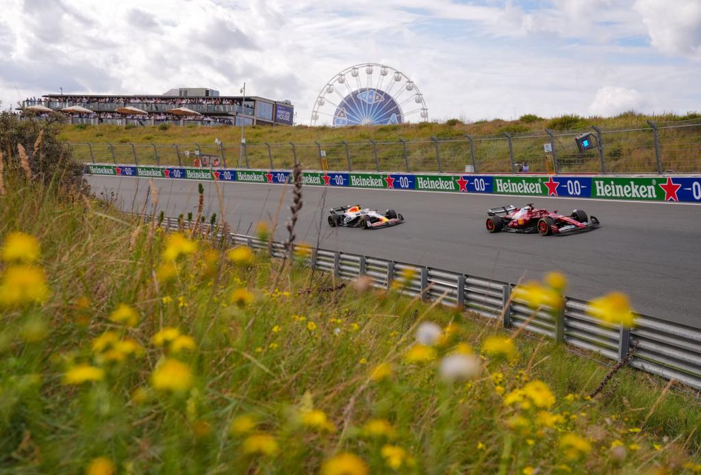 Charles Leclerc's Ferrari with the Racing Bulls of Isack Hadjar behind him. In the foreground are flowers on the field next to the Zandvoort circuit