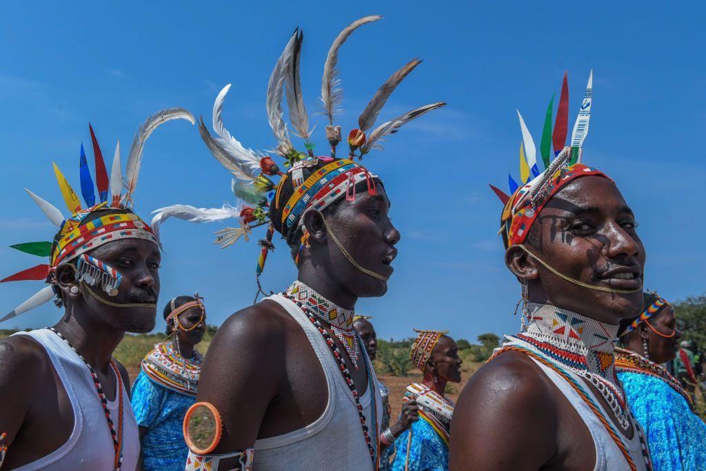 Three men from the Rendille community wearing brightly beaded jewellery and feathered headdresses. 