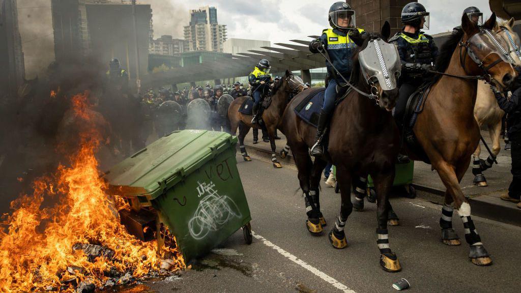 Mounted police ride past flaming bins in Melbourne