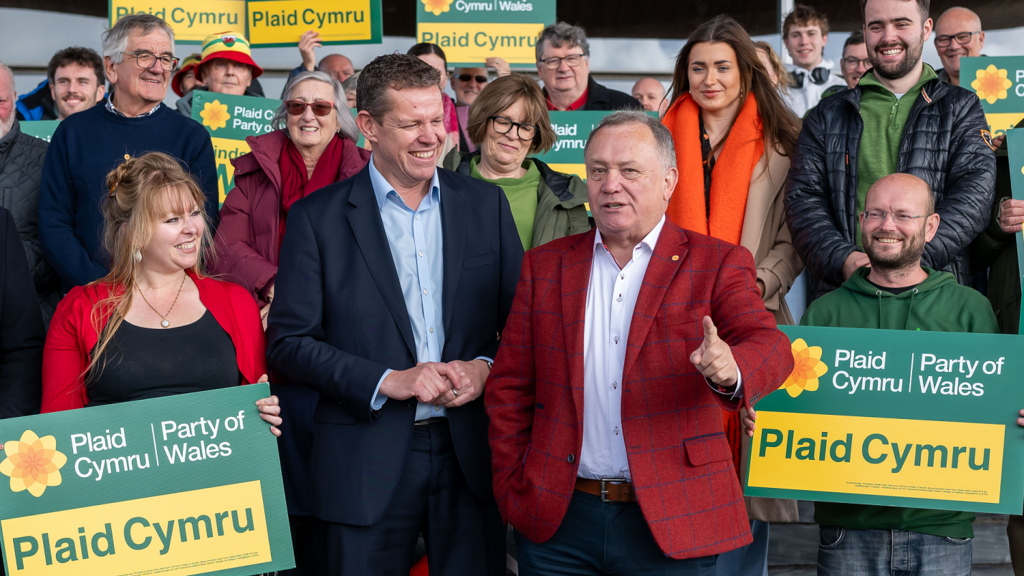 Lindsay Whittle and Rhun ap Iorwerth on the steps of the Senedd, they are surrounded by Plaid supporters holding placards and smiling