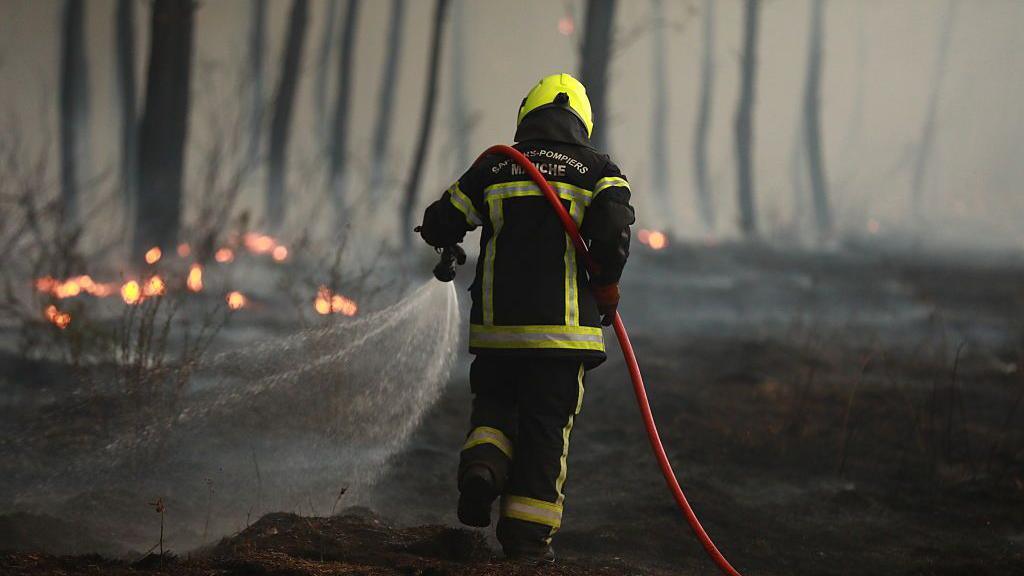 A firefighter carrying a hose spraying water on a fire