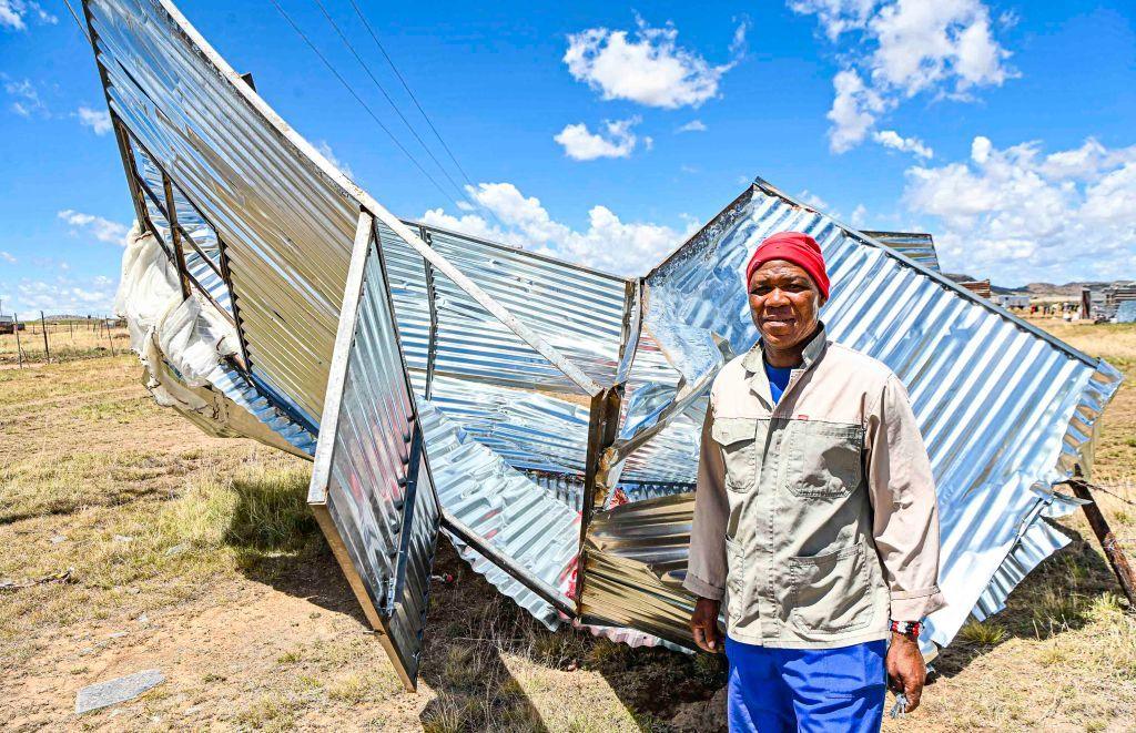 A man stands next to a pile of corrugated iron that was once his home.