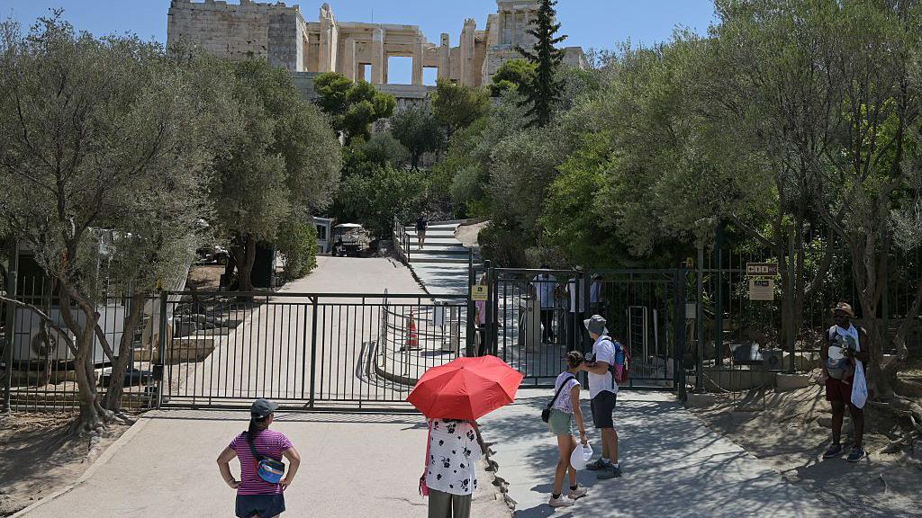 people standing outside shut gates of the ancient monument of the Acropolis in Athens