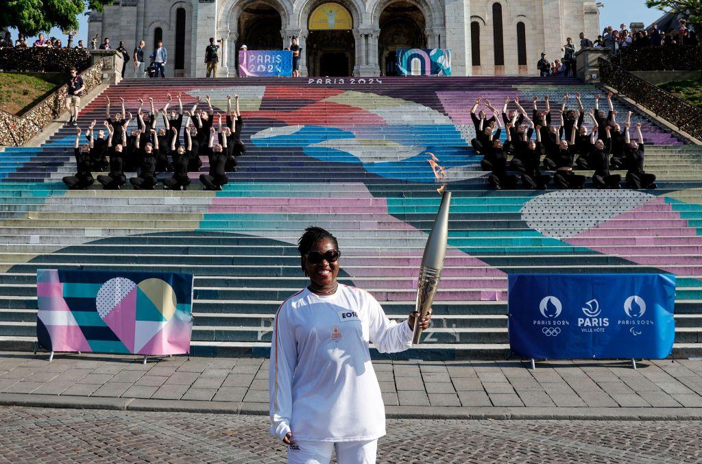 A woman holds the Olympic torch and smiles.