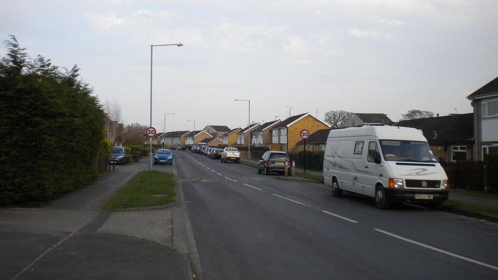 A residential street with house, streetlamps and parked cars