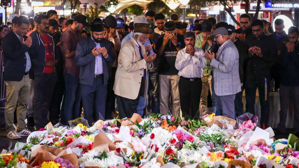 Members of the Ahmadiyya Muslim Community of Australia offer prayers in front of flowers left outside the Westfield Bondi Junction shopping mall