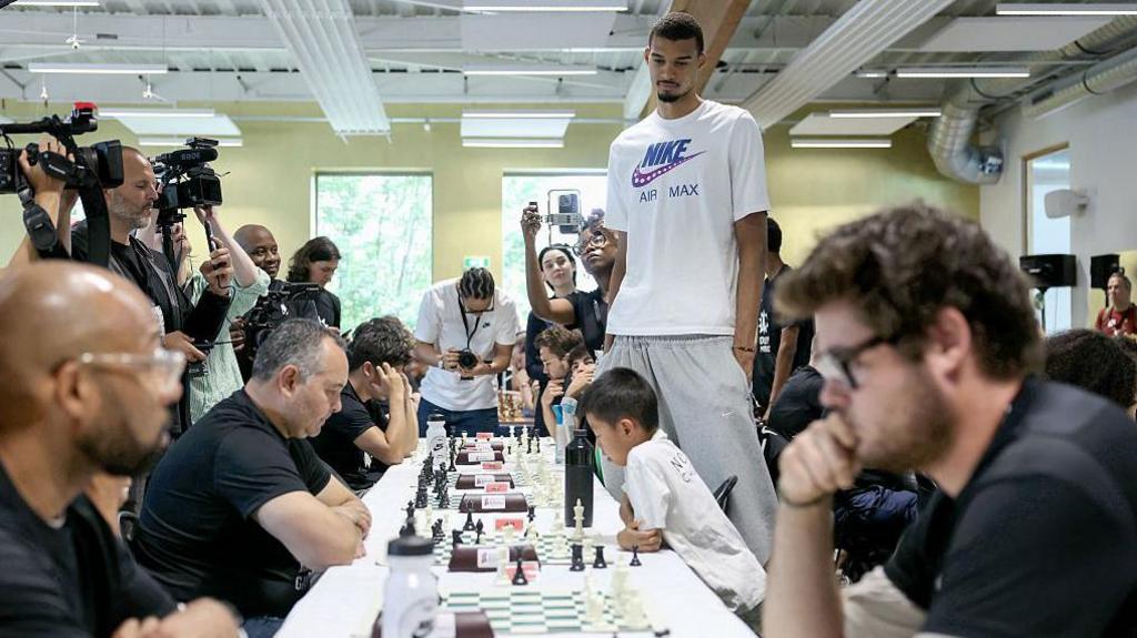 Victor Wembamyama watches a table of people playing chess