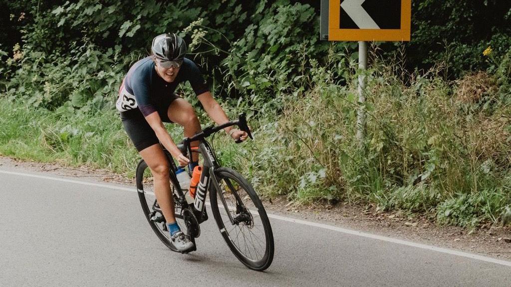 Angela Mills-Bannon on a bike pedalling around a corner on a road.