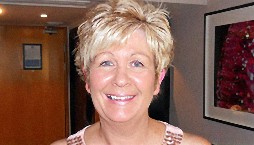 A blonde haired woman smiles for the camera while standing indoors