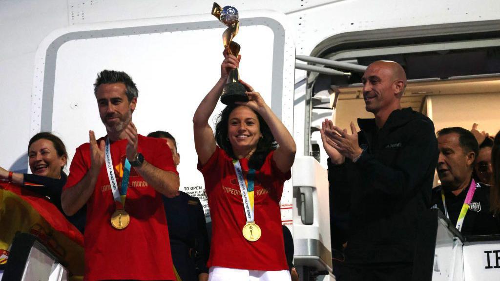 Spain women's national football player Ivana Andres holds up the World Cup trophy next to Spain's manager Jorge Vilda (L) and Spanish football federation president Luis Rubiales (R)