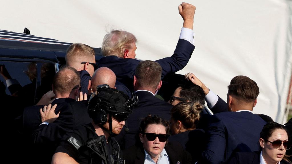 Donald Trump raises his fist after being shot in the ear, which is bleeding, as Secret Service agents move him away.