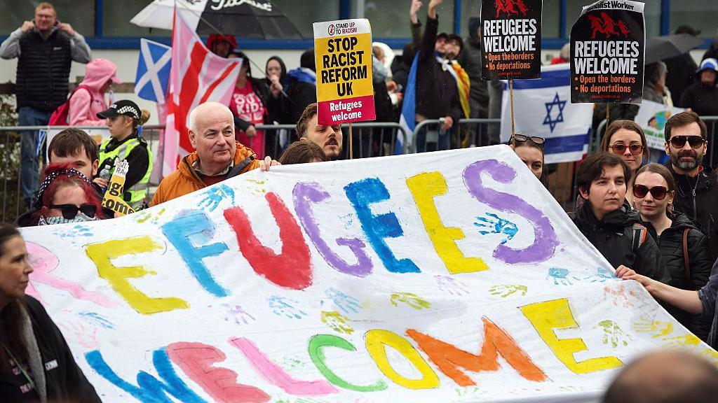 Counter-protestors at the hotel hold a banner reading Refugees welcome.