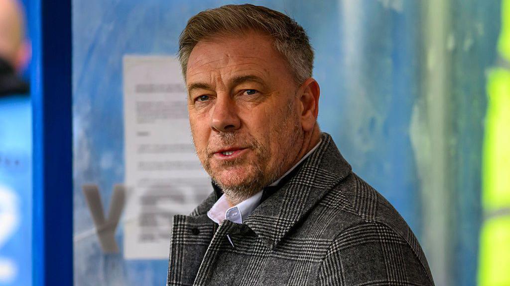 Crawley Town boss Scott Lindsey looking at the camera wearing a grey checked coat