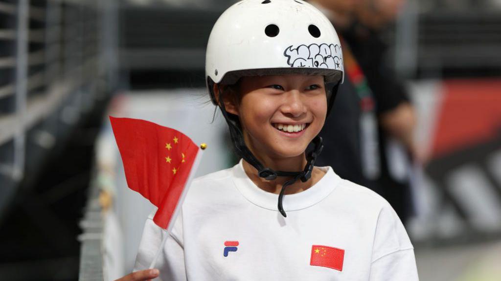 A picture of young skateboarder Haohao Zheng wearing a white helmet and waving a flag of China