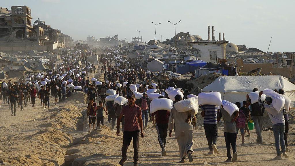 Palestinians walk carrying white bags of food aid in Gaza
