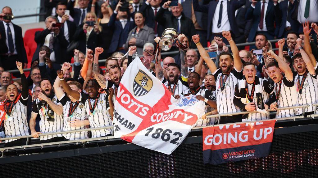 Notts County players look nervous while linking arms as they watch the penalty shootout from the halfway line during their victory over Chesterfield in the 2022-23 National League play-off final