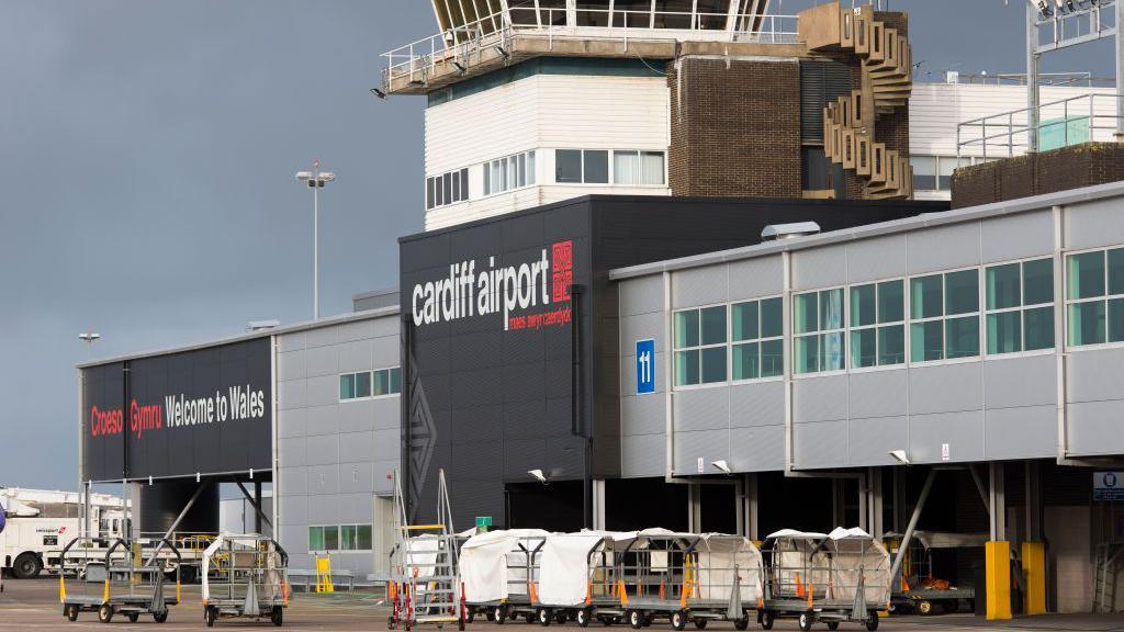 A general view of Cardiff Airport main terminal building. It is grey and black, with the words Welome to Wales in English and Wales on the side. 