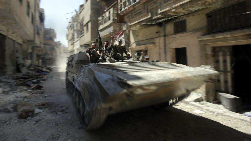 A tank drives through ruined streets