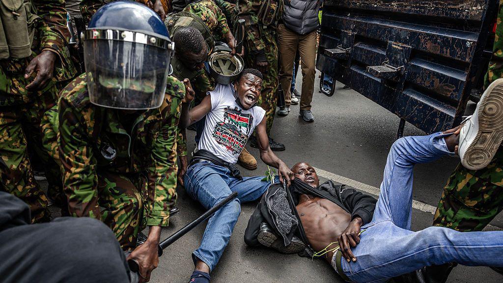 Security forces in military fatigues appear to be detaining two protesters, who are both on the ground