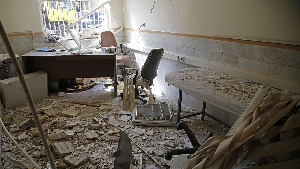 A view of Evin prison is seen in the wake of an Israeli strikes on the site in June. A cot can be seen covered in debris, and rubble covers the floor. A barred window is seen with light shining through it. Wires hang from the walls and ceiling.
