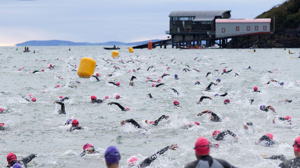 People in wetsuits swimming in the sea in front of a lifeboat house