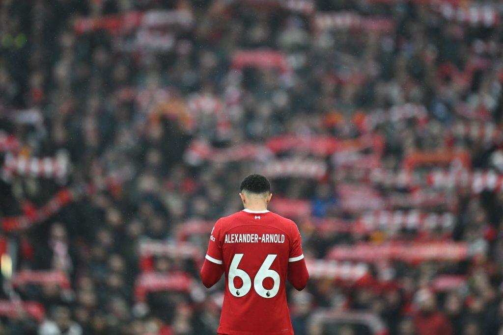 Trent Alexander-Arnold stands on the Anfield turf before kick-off as fans raise scarves in the background.