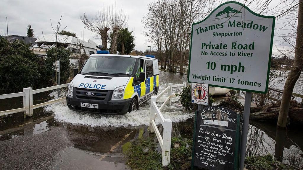 A police van driving through a flooded area in Thames Meadow, Shepperton