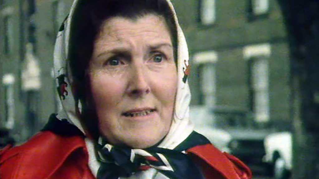 A close up of a lady wearing a headscarf and red coat.