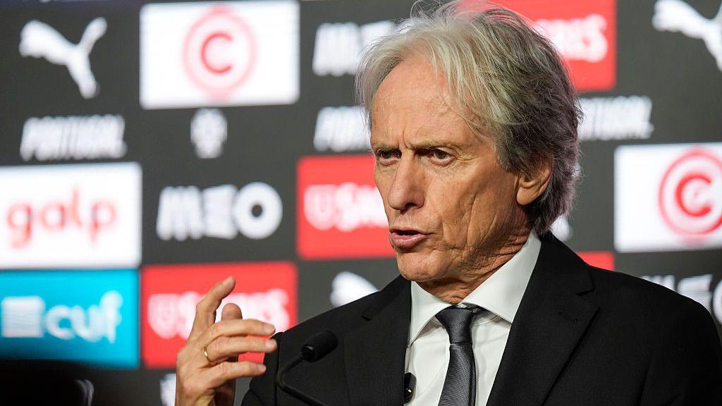 Jorge Jesus, wearing a black suit, gesticulates with his right hand while speaking at a press conference 