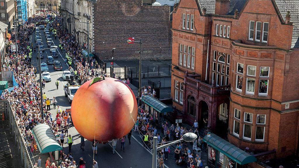 Members of the public gather to watch a giant peach as it is moved through the centre of Cardiff as part of a street performance to mark the start of City of the Unexpected, a celebration of the author Roald Dahl.