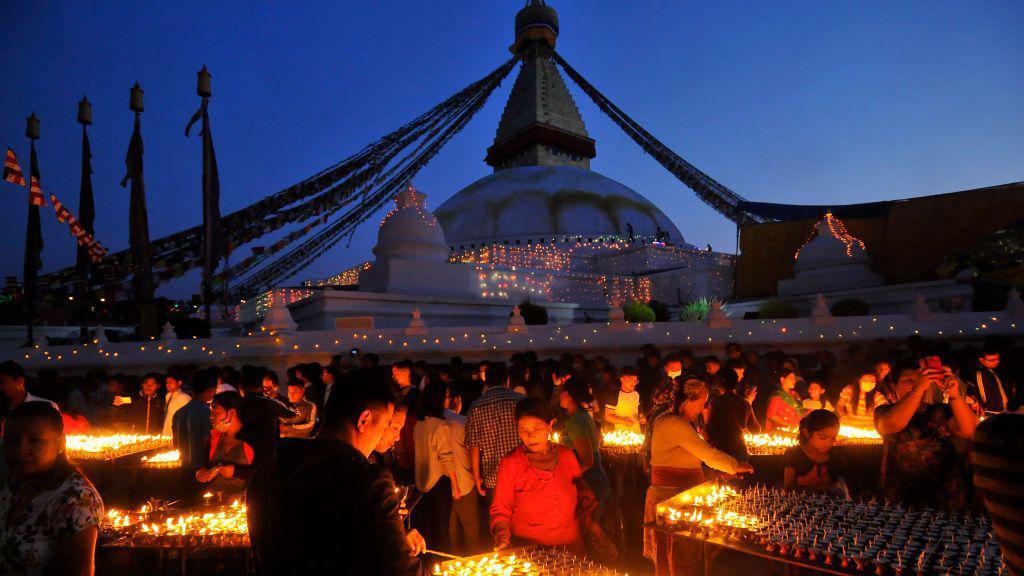 Buddhists light small candle lamps outside a temple.