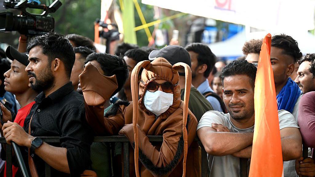A group of people, some looking at the camera, at the protest site in Jantar Mantar. One person in the centre is wearing a brown cockroach costume with long, drooping ears.