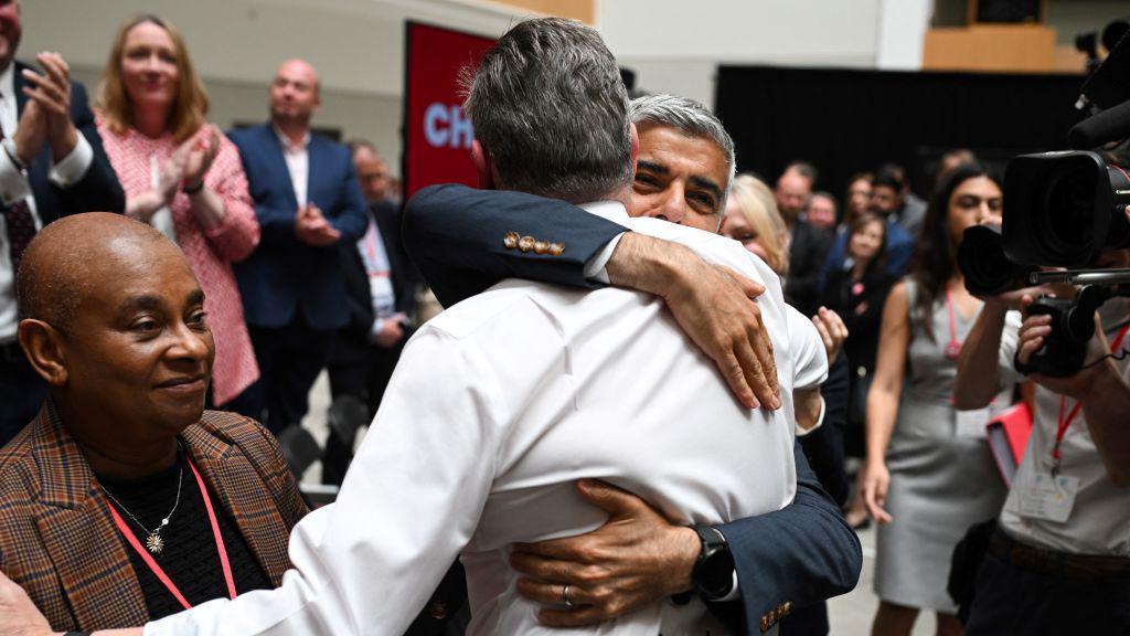 Mayor Sadiq Khan hugs Sir Keir Starmer while people  including Baroness Lawrence look on