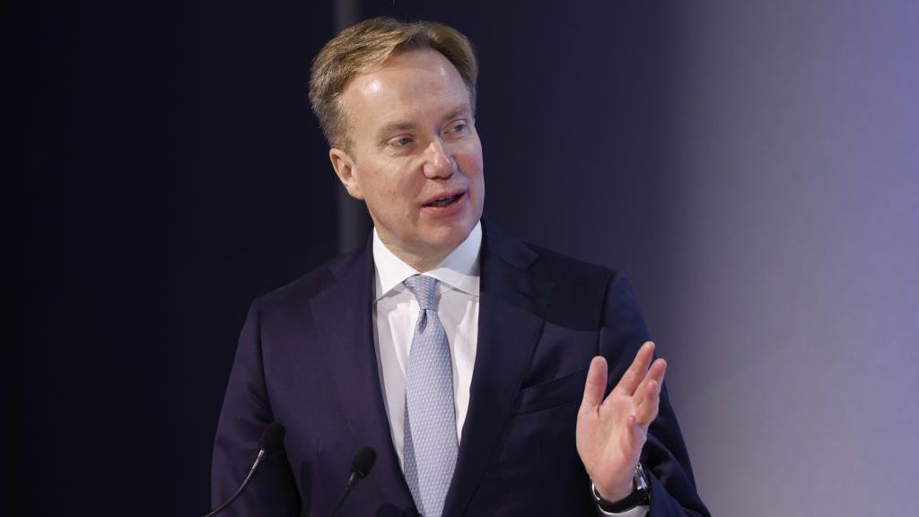 Borge Brende, president of the World Economic Forum, speaks in front of two small microphones, wearing a navy blue suit