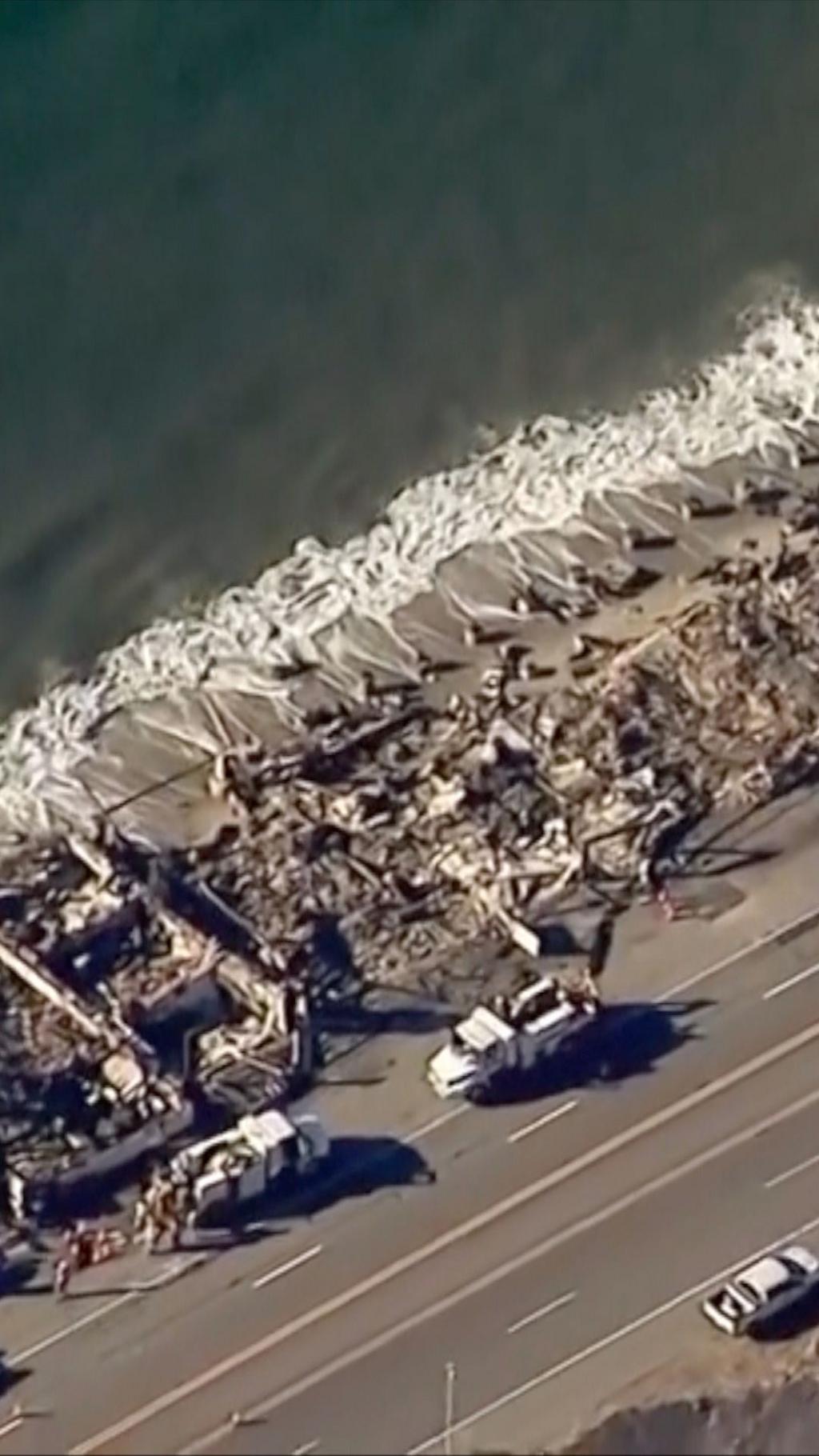 Destroyed buildings as seen from above, next to a road and the sea